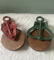 Two cast metal and wood barn pulleys shown top-down, red and green colored metal frames with round wooden wheels.