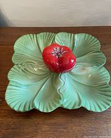Top view of green ceramic lettuce leaf plate with attached lidded red tomato pot in center.