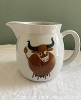 Front view of white ceramic milk jug with brown cow design.