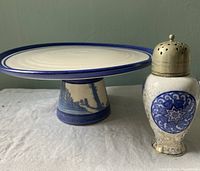 Cake plate with blue rim and scenic base next to crackled white sugar shaker with blue Osaka medallion and metal lid