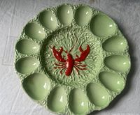 Full view of green ceramic egg plate with red lobster in the center and twelve oval egg places around the edge.