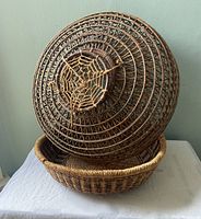 Photo shows the woven fish trap placed upside down on the woven basket to display the shape and weaving detail of both items.