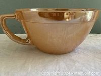 Side view of peach lustre Fire-King batter bowl showing handle and shiny surface with some scratches.