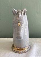 Front view of white horse-shaped vase with gold fleck details and gold nose accent on a beige surface with green wall background.