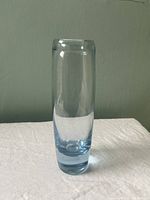 Front view of the tall cylindrical ice blue glass vase on a white cloth against a neutral wall.