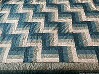 Close-up view of the quilt showing the Rail Fence pattern with various shades of blue and green fabric strips and hand quilting details.