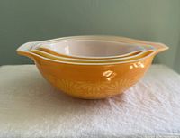 Side view of three stacked Pyrex Cinderella bowls showing orange-yellow daisy pattern and spouts.