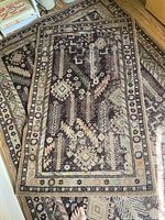 Photo showing the smaller 3'x5' wool rug with geometric and botanical pattern, placed on wooden floor near furniture and books