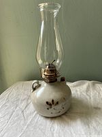 Front view of signed Loos pottery oil lamp showing ceramic base with floral pattern, glass chimney, and metal burner.
