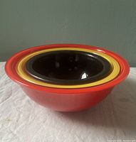 Side and top stacked view of the four Pyrex nesting bowls showing red, yellow, black, and green bowls nested inside each other on a white cloth against a green wall.