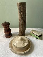 All four items laid out on white fabric: tall wooden pepper mill with bark, rustic wooden grinder, VW van salt shaker in green and white, cream covered butter dish with lid