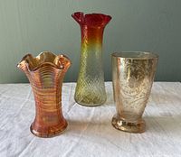 Overview of three mini vases including iridescent ruffled Marigold vase, pressed glass tumbler with etched floral pattern, and red-yellow fluted rim vase.