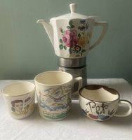 Vintage floral ceramic stovetop espresso/mocha pot with a white ceramic top decorated with large pink roses, blue and yellow flowers, paired with three small retro espresso mugs showing different designs including 'Pops' with floral motif.