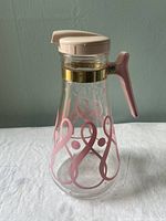 Full view of the E-Z Por vintage juice pitcher showing clear glass body with pink ribbon design, pink handle, plastic lid, and metal band.