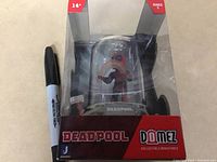 Clear view of unopened Deadpool Domez collectible figure box with a marker beside for scale.