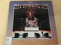 Front cover of Rush All The World's A Stage vinyl LP showing stage with instruments and star background