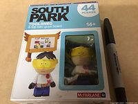 Front of South Park McFarlane Toolshed figure box with figure visible in clear window and packaging showing 44 pieces and age 14+. Next to a marker for scale.