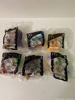 Six sealed McDonald's collectible toys from Beauty and the Beast displayed together in original packaging.