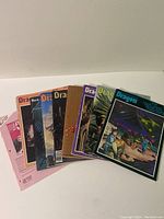 Display of seven Dragon Magazine issues fanned out showing various colorful fantasy and sci-fi covers along with a pink player record sheet.