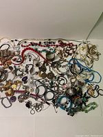 Photo showing a large pile of assorted bracelets and necklaces including beaded pieces, metal bangles, and charm bracelets in various colors.