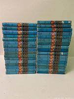 Large stack of 31 vintage Hardy Boys hardcover novels in blue dust jackets, mostly spines showing titles and colorful Hardy Boys illustrations