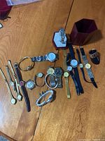 Overview photo showing a collection of 17 vintage wristwatches and one ring arranged on a wooden table.
