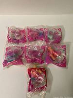 Photo showing seven My Little Pony toys individually wrapped in original McDonald's packaging, displayed on a plain surface.