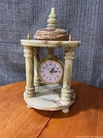 Full view of onyx stone clock with circular top supported by turned pillars and dome finial on top.