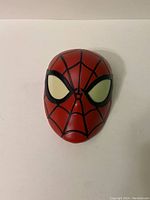 Front view of red and black Spider Man mask-shaped night light with white eyes.