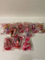 Photo of eleven new Strawberry Shortcake McDonald's toys, each in original sealed plastic bags showing red McDonald's 'M' and strawberry graphics.