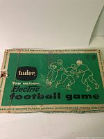 Original green Tudor Tru Action Electric Football game box showing logo and football player graphics with some damage and wear.