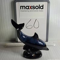 Blue ceramic dolphin figurine with dark blue glaze and black base photographed with a ruler for size reference, front view.