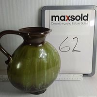 Front and side view of Blue Mountain Pottery 8.25-inch vase showing pale green glazed bulbous body with dark brown rim and handle. No chips or cracks visible, showing minor surface wear.