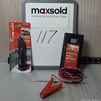 Photo showing Speedrite digital volt meter with red and black test wires and an orange alligator clip, and unopened Accutire digital tire gauge in packaging.
