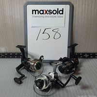 Three used spinning reels by Shakespeare including one Alpha 035 and two Performance Series models arranged on a table with a MaxSold sign.