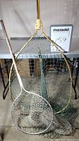 Photo showing the pair of fishing dip nets with the larger one placed behind the smaller one, showcasing netting condition, handles, and hoop sizes.