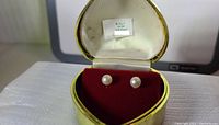 Photo of two freshwater pearl stud earrings set in sterling silver posts inside a yellow and red velvet jewelry box.