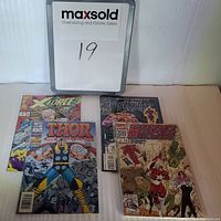 Four Marvel comics displayed on a table with a MaxSold placard numbered 19. Titles visible are X-Force, Thor Corps, Night Thrasher, and Southern Squadron.