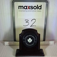 Front view showing the official Toronto Maple Leafs hockey puck mounted on a dark wooden plaque with ruler for size reference.