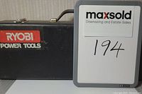 Closed black metal case with Ryobi Power Tools logo and metal latches, seen from front with carrying handle on top.