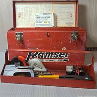 Front view of Ramset metal toolbox with open lid and various hand tools displayed in front compartment, including Black & Decker staple gun and hand saw.