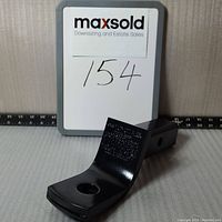 Side view of black metal Toyota trailer hitch ball mount with number 154 on a white board behind it.