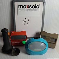 Front view of three View-Master devices in orange, beige, and blue colors with two black vintage phone mouthpieces on a white surface.