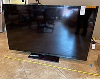 Front view of Samsung 60" TV on floor with remote placed in front."