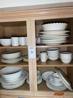 Two cupboards showing two different Arcopal France China dining patterns, with a variety of mugs, bowls, plates, and serving dishes stacked neatly on shelves.