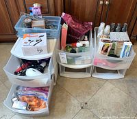 Wide shot showing three sets of plastic drawers filled with hair styling and personal care items including hairdryers and curling irons, unopened boxes and bottles.
