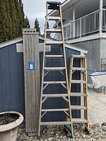 Photo of the three items showing a large 10ft step ladder, a shorter 6ft step ladder, and an 8ft long collapsible platform leaning against a blue wall outside.
