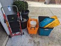 Full lot showing red metal hand truck/step stool combo next to orange, blue, yellow and black plastic storage bins and a white bucket inside the orange bin.