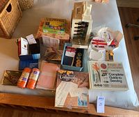 Photo showing full lot spread on table including sewing kit with threads, scissors, scrapbooking kit, calligraphy set, Reader's Digest sewing guide, yarn skeins and fabric swatches.