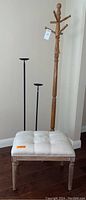 Full view of cushioned stool, wooden coat rack, and two black metal candle holders showing general wear and repair on coat rack leg
